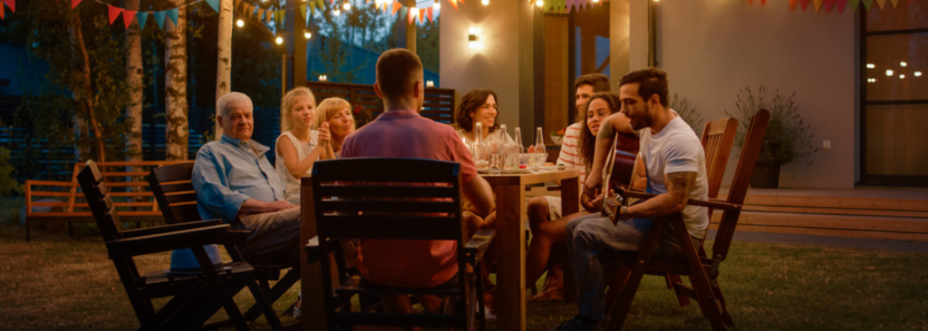 Am Dinner-Tisch sitzend, spielt der junge Mann Gitarre für einen Freund. Familie und Freunde Musik hören bei der Sommerabendfeier.